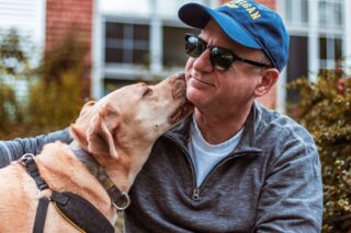 A dog licking the face of a retired man.